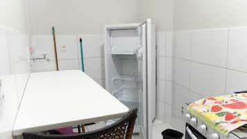 A small, compact room with a white table, a chair, a refrigerator, and a stove.