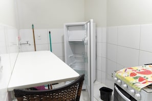 A small, compact room with a white table, a chair, a refrigerator, and a stove.