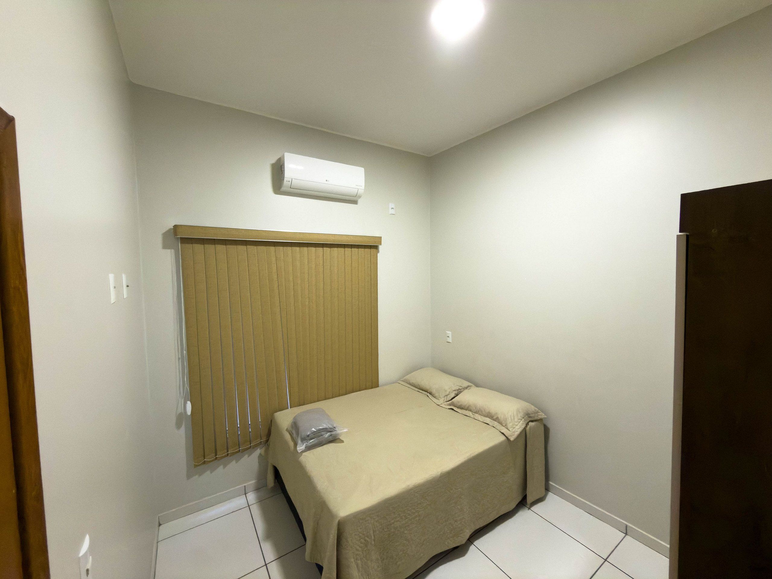 Una habitación pequeña con una cama individual, cabecera de madera, unidad de aire acondicionado blanca en la pared y una puerta cerrada.