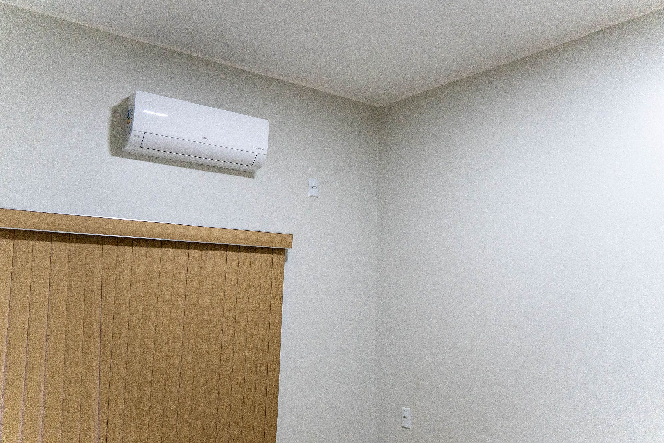 Una habitación con un aire acondicionado blanco montado en la pared, una puerta de madera y una pared lisa con un interruptor de luz.