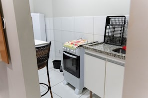 A compact kitchen with a stove, sink, and a small trash bin.