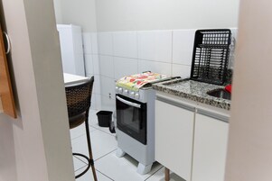 Cozinha compacta com fogão, pia e lixeira pequena.