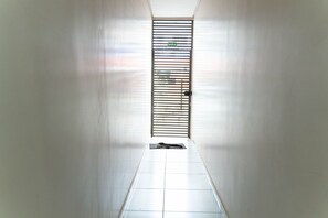Un pasillo con una puerta al final, piso de baldosas y una verja metálica con un letrero encima.