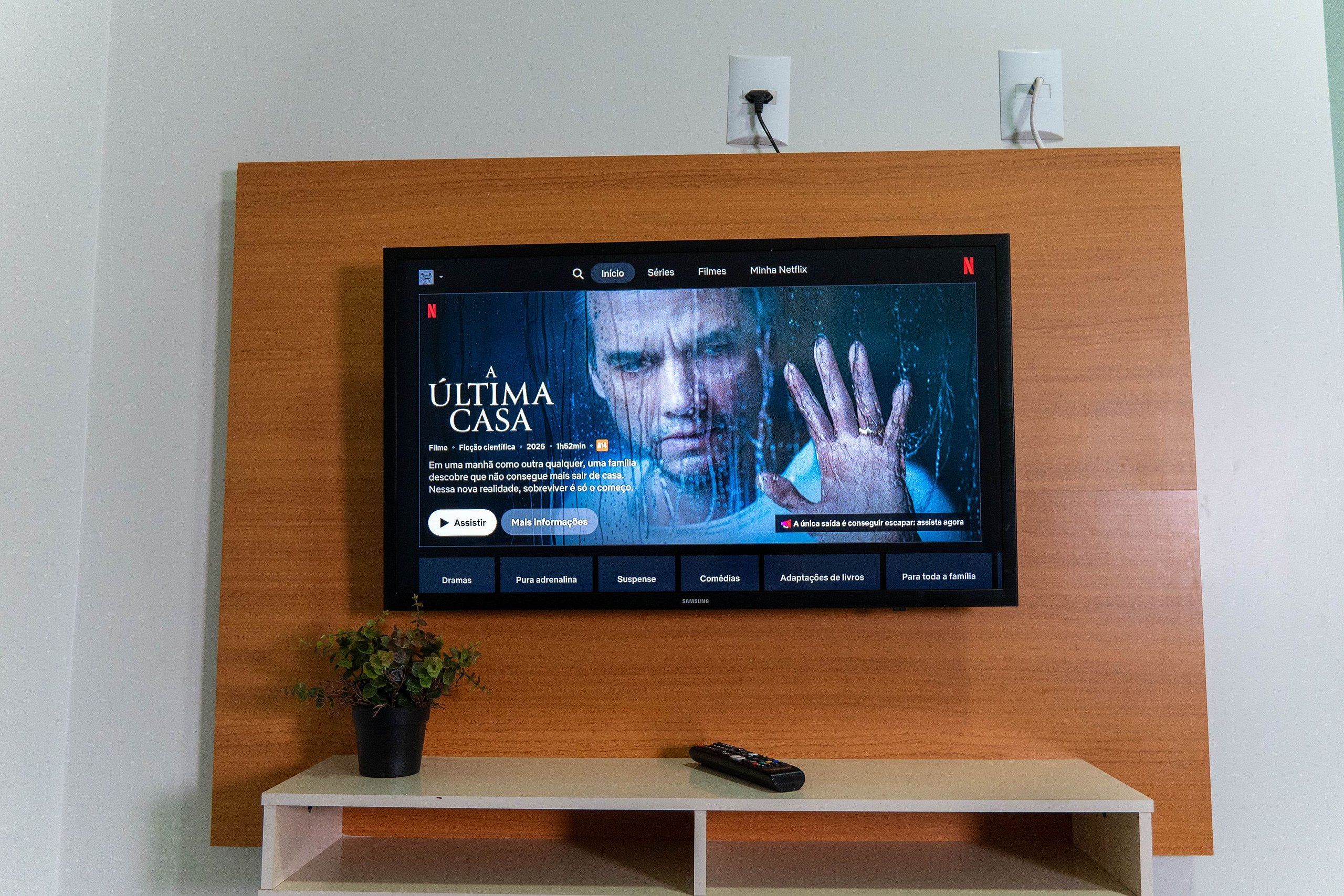 Un televisor montado en una pared de madera con un control remoto sobre un pedestal blanco debajo.