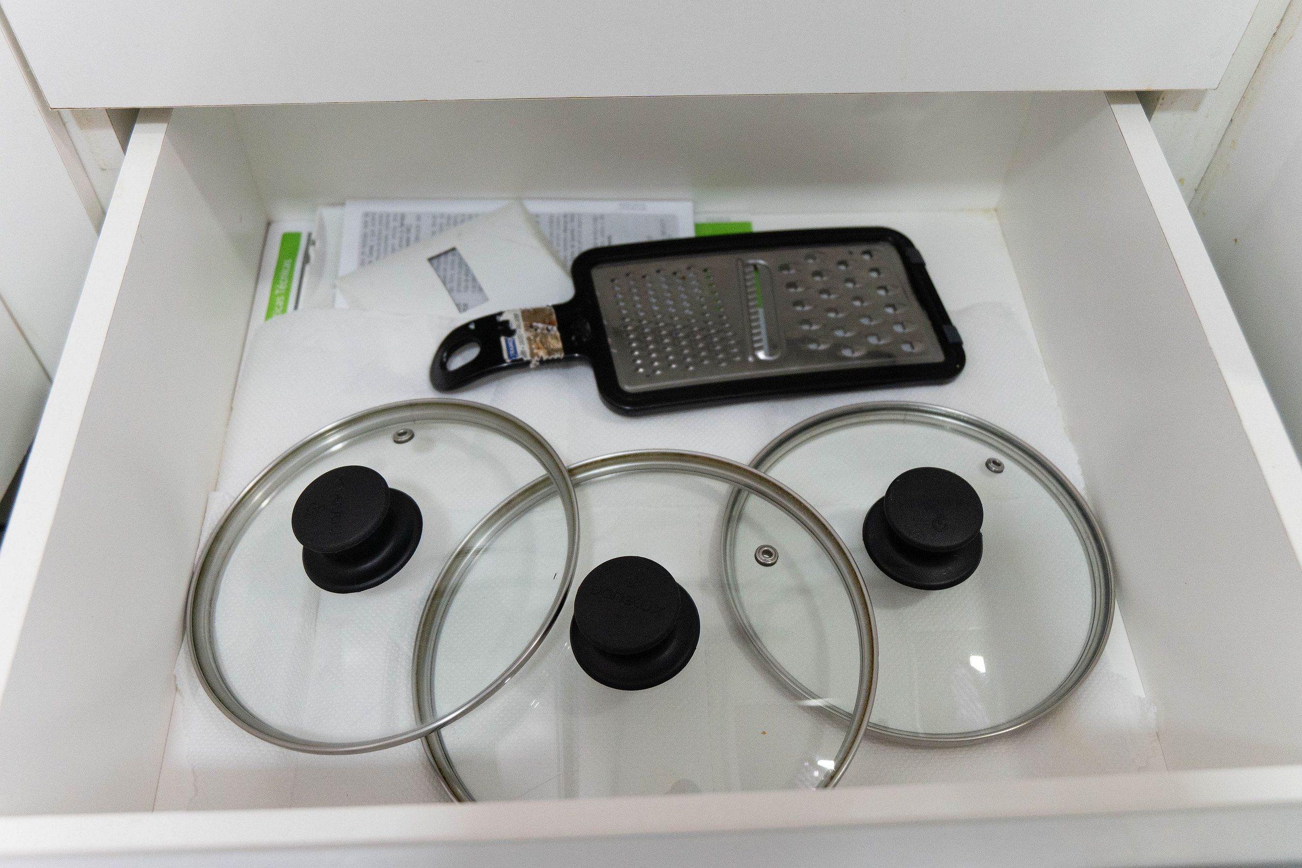 Un tiroir contenant un appareil électronique noir, qui pourrait être une râpe, ainsi que trois couvercles en verre transparent munis de boutons noirs.