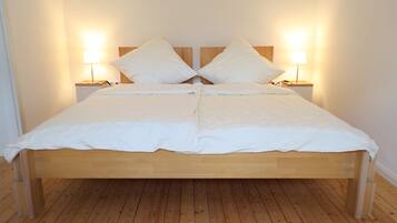 Ein Doppelbett mit Holzrahmen und weißer Bettwäsche, flankiert von zwei Nachttischen mit Lampen, in einem Raum mit Holzboden.