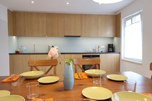A modern kitchen with wooden cabinets, a dining table set with yellow plates, and a vase with a flower.