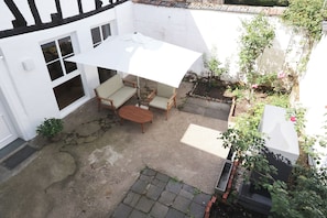 A patio with a table and chairs, a white umbrella, and a garden with plants and a brick border.