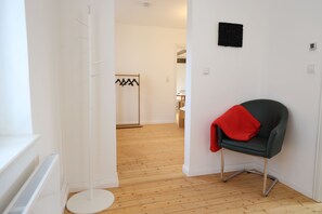 A hallway with a coat rack, a chair with a red cloth, and a wooden floor.