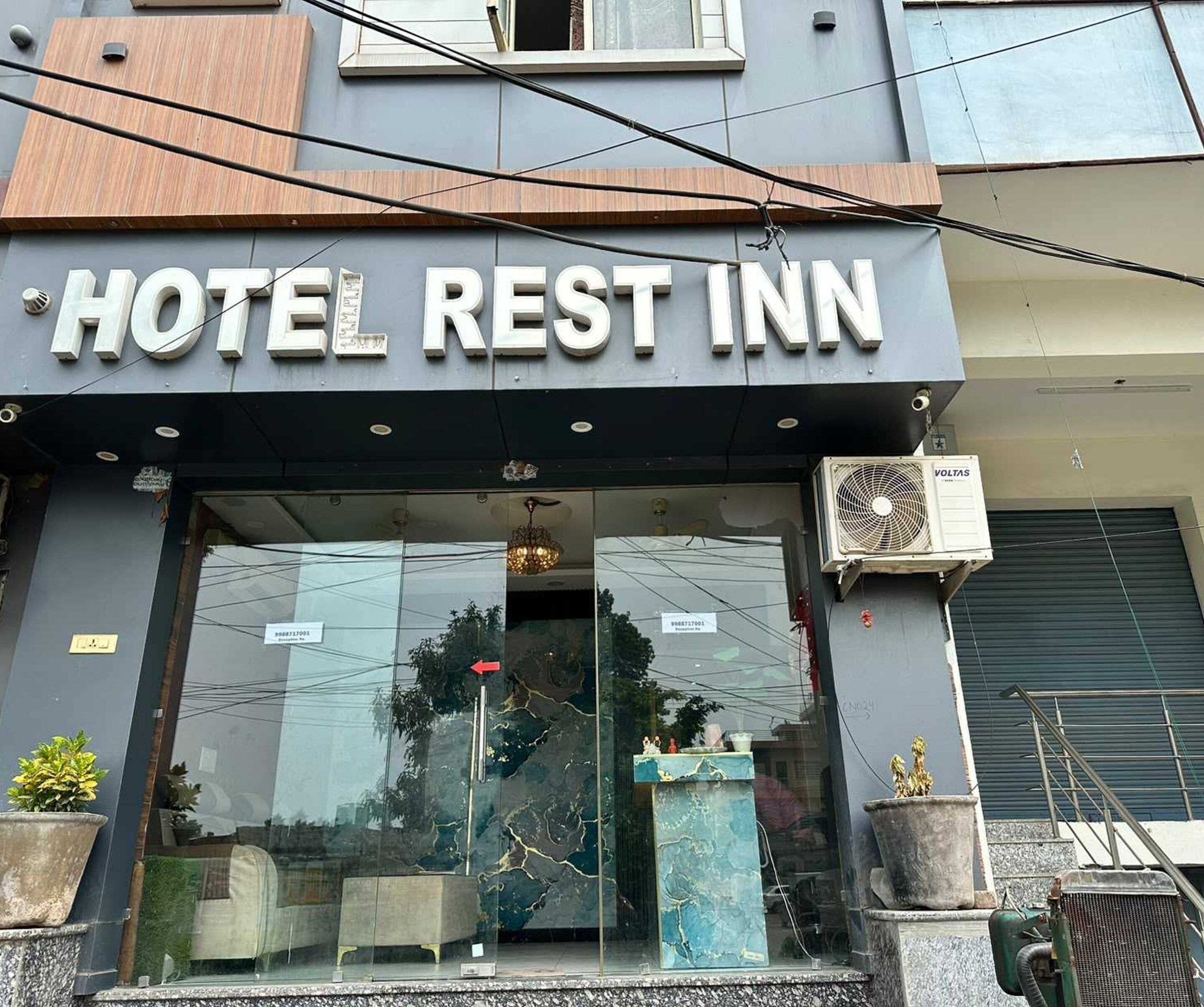 A hotel named 'HOTEL REST INN' with a modern facade, large glass entrance, and outdoor potted plants.