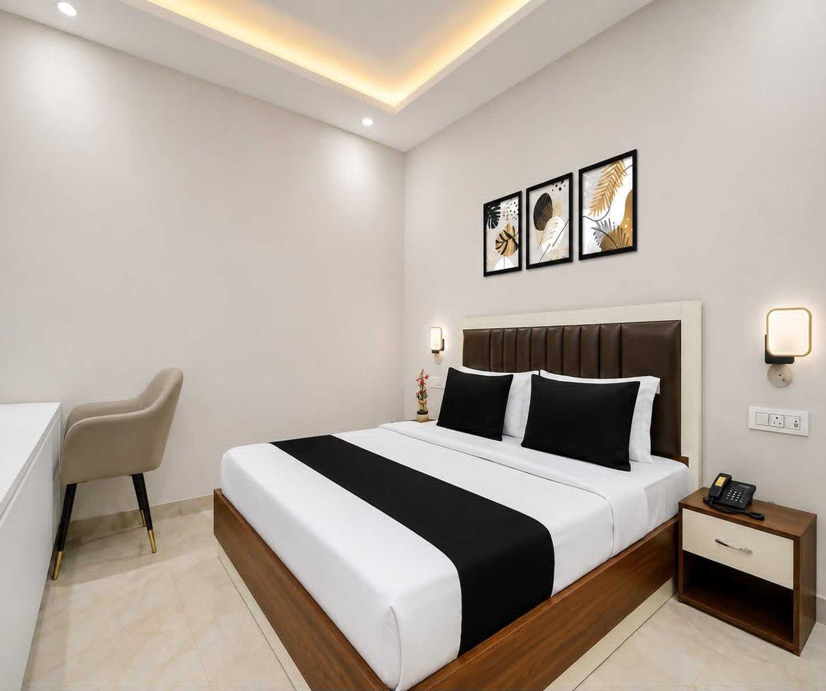 A hotel room with a bed, bedside table, chair, and artwork on the wall.