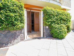A building entrance with a stone wall, a wooden door, and a sign indicating a parking area. - 1-bed Suite With Private Patio (Trecastagni)
