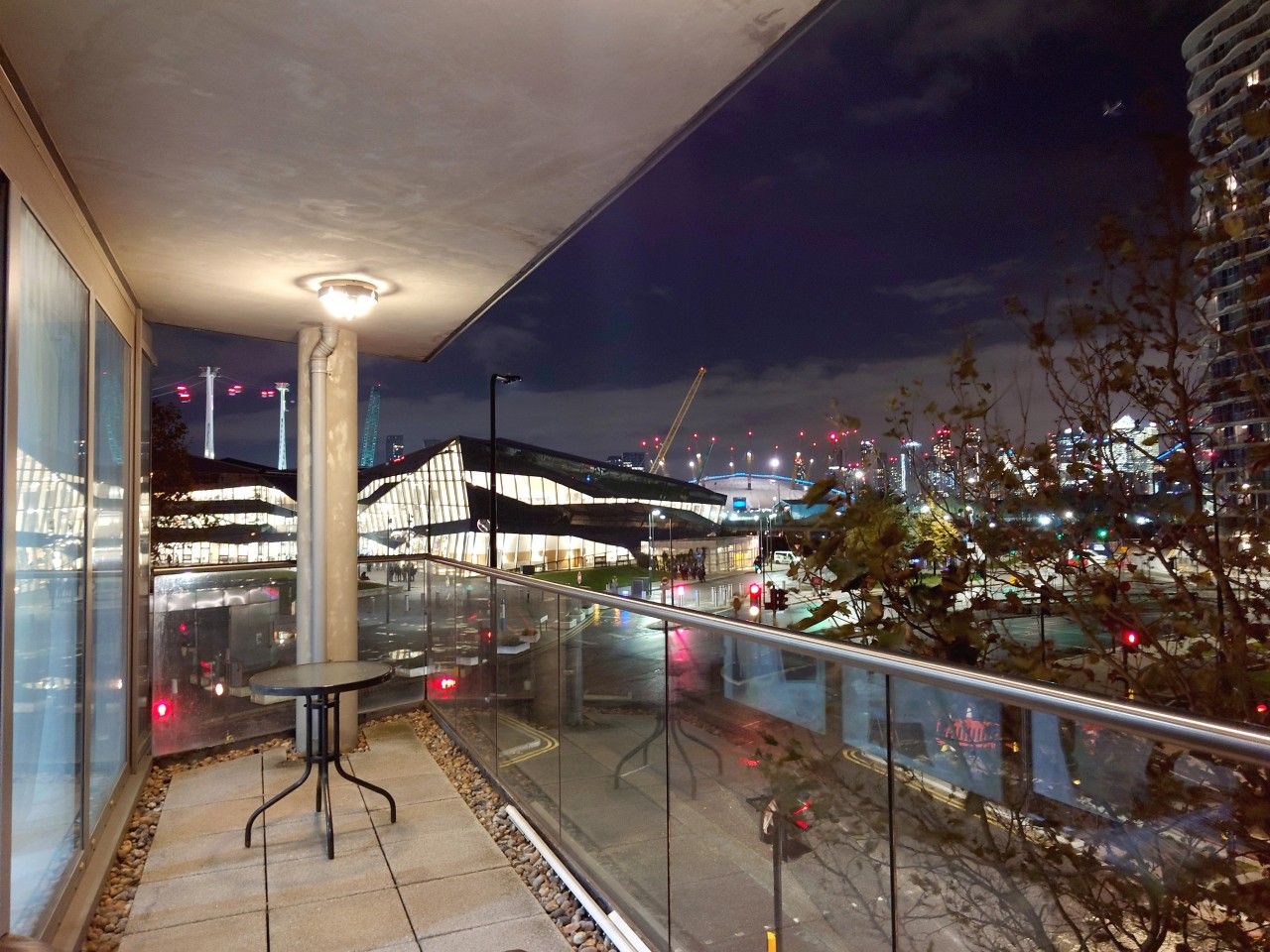 A balcony with a glass railing overlooking a cityscape at night.