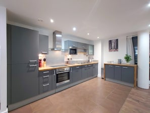 A modern kitchen with grey cabinets, stainless steel appliances, and a wooden countertop. - Modern 2-Bedroom Apartment Near ExCeL London (London)