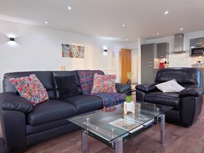 Uma sala de estar moderna com um sofá de couro preto, uma mesa de centro de vidro e uma poltrona de couro.