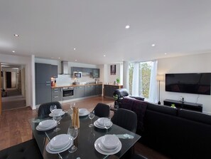 A modern living space with a dining area, kitchen, and a large TV screen. - Modern 2-Bedroom Apartment Near ExCeL London (London)