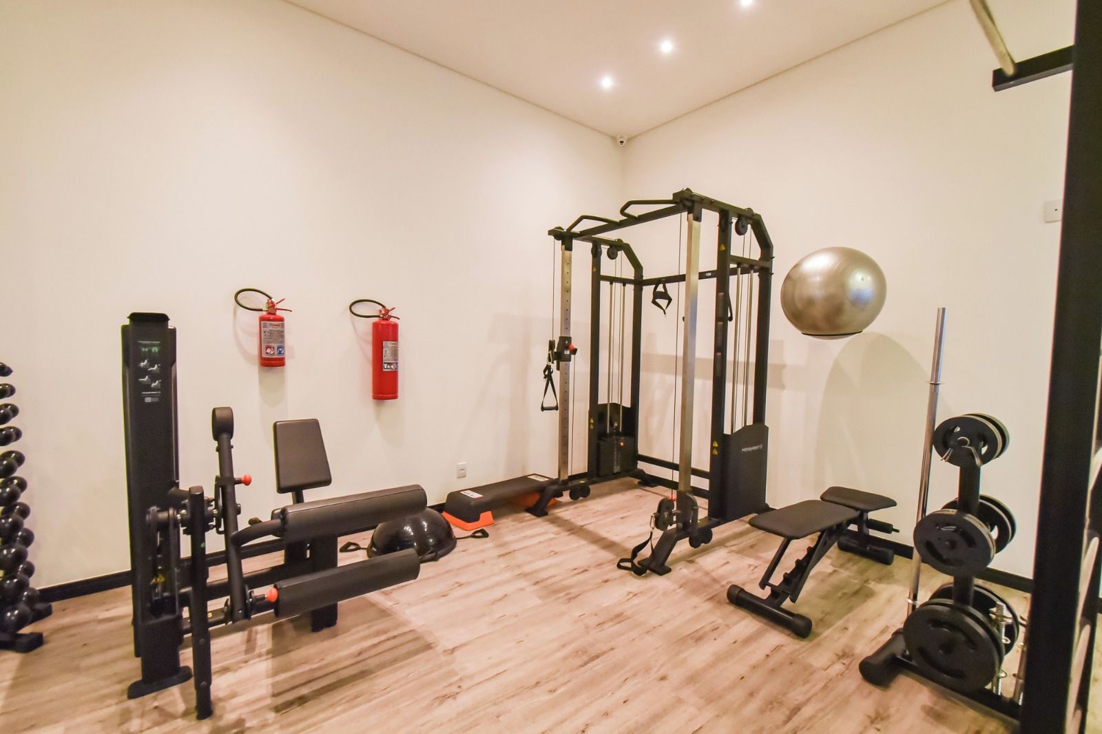 Een sportschool met diverse fitnessapparaten, een brandblusser en een spiegel.