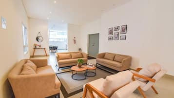 Un vaste espace de vie comprenant plusieurs canapés et une table basse, un coin repas avec des chaises, et une porte donnant sur une autre pièce.