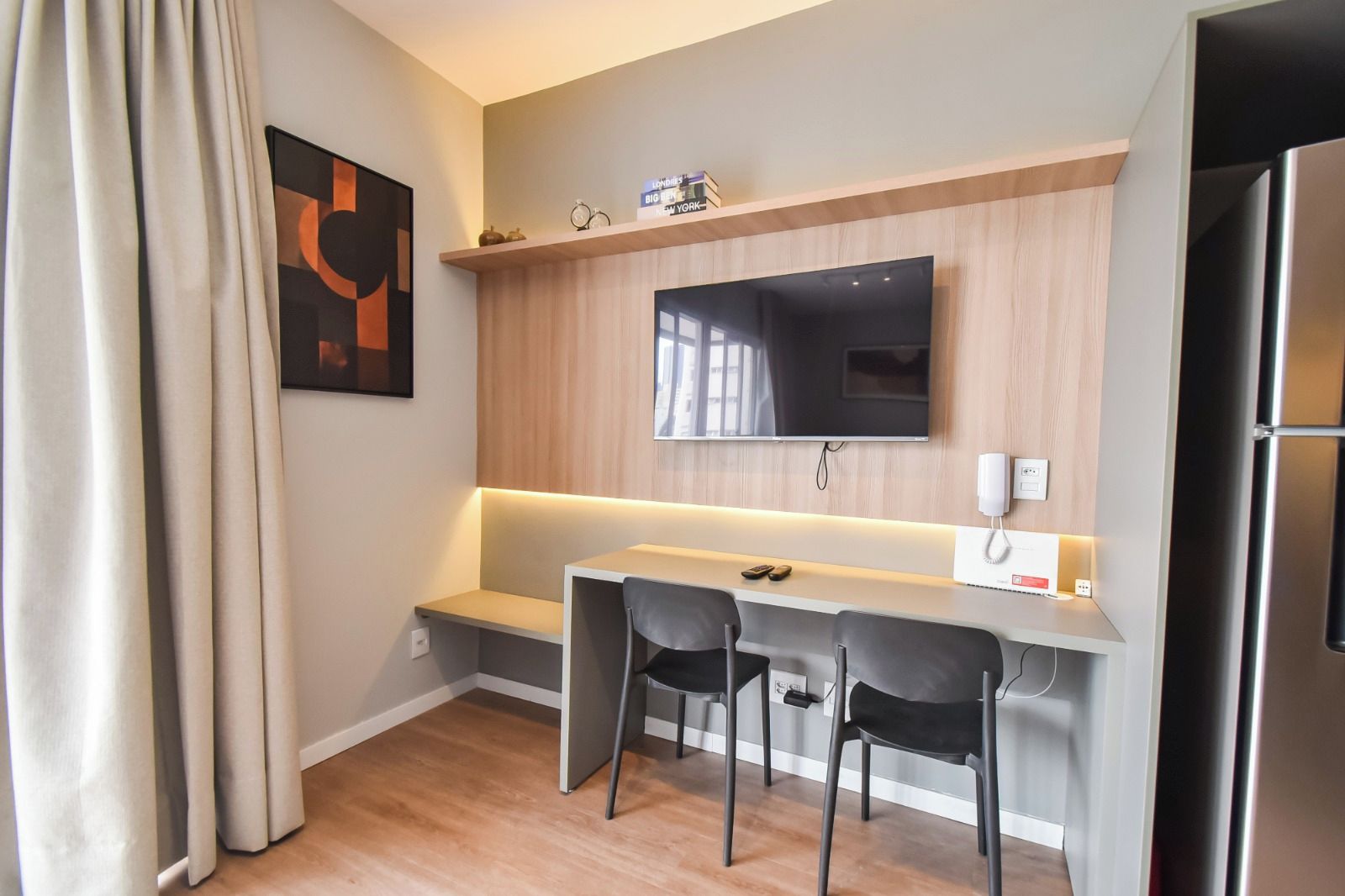 Une chambre d’hôtel moderne dotée d’un téléviseur à écran plat fixé sur un mur en bois, d’une petite table avec deux chaises et d’un réfrigérateur.