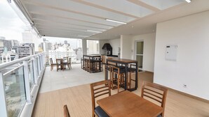 A balcony with a wooden floor, a dining table with chairs, and a kitchen area with a stove. - StayHome Rua Augusta - Heated Pool & Gym (São Paulo)