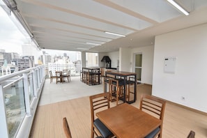 A balcony with a wooden floor, a dining table with chairs, and a kitchen area with a stove. - StayHome Rua Augusta - Heated Pool & Gym (São Paulo)