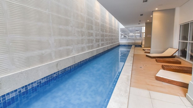 A swimming pool with a tiled edge, adjacent lounge chairs, and a wall with a textured pattern. - StayHome Rua Augusta - Heated Pool & Gym (São Paulo)