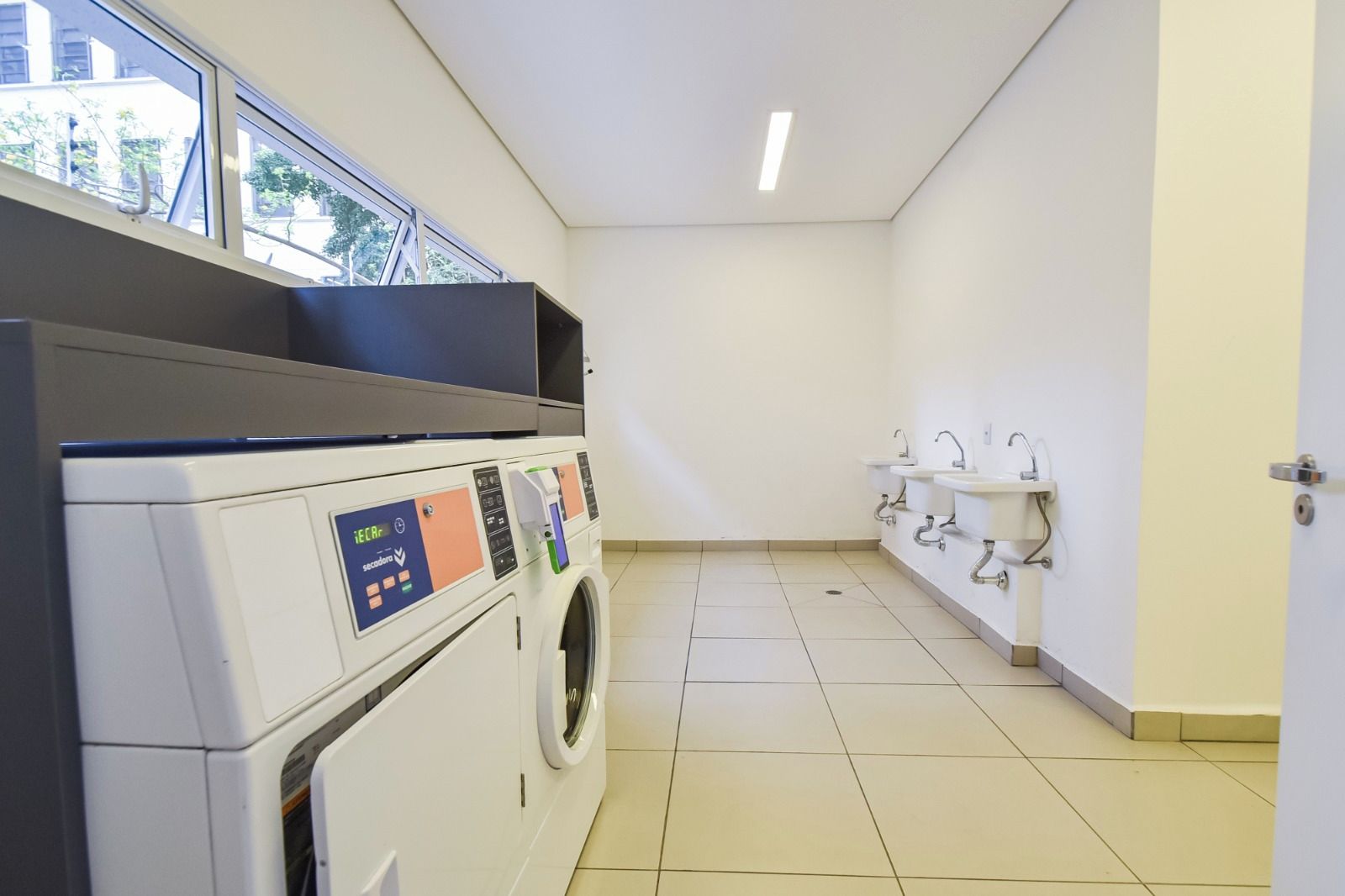 Une buanderie équipée d’un lave-linge et de sèche-linge, d’un espace avec un évier et d’une fenêtre donnant sur l’extérieur.