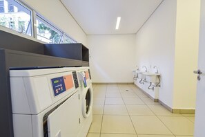 A laundry room with a washing machine and dryers, a sink area, and a view of the outside through a window. - StayHome Rua Augusta - Heated Pool & Gym (São Paulo)
