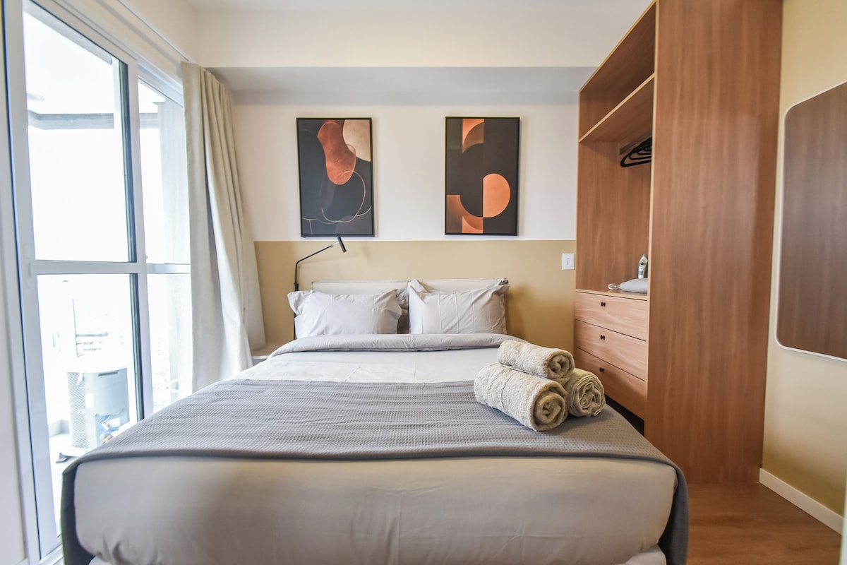 A hotel room with a large bed, a wardrobe, and two abstract paintings on the wall.