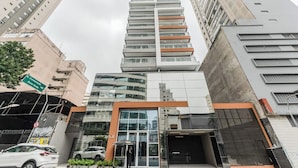 A multi-story building with a glass facade, a ground-level entrance with a canopy, and a visible staircase leading to the entrance. - StayHome Rua Augusta - Heated Pool & Gym (São Paulo)