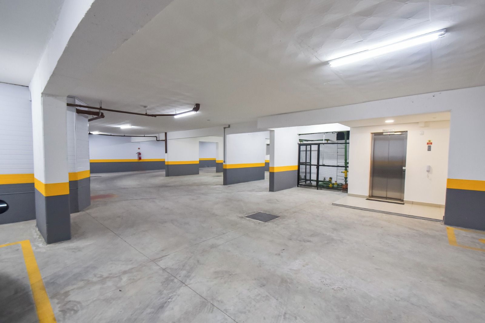 Garagem de estacionamento com vários níveis, pisos de concreto e pilares amarelos e cinzas.