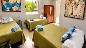 A room with two beds, each with a green bedspread and blue pillows, a wooden wardrobe, and a window with a view of greenery. - Villaggio 2 (São Sebastião)