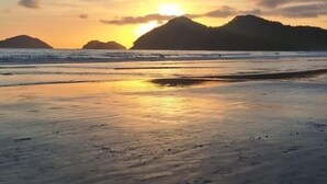 A beach with a sunset, calm sea, and distant hills. - Villaggio 2 (São Sebastião)
