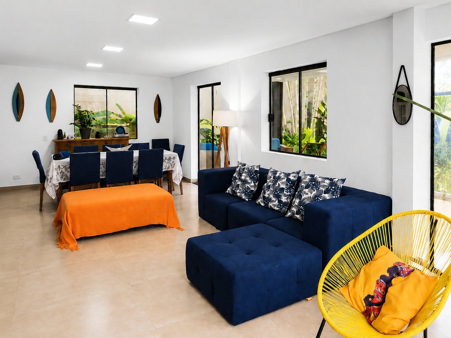 Uma sala de estar moderna com um sofá, um banquinho e uma poltrona amarela. Há também uma área de jantar com mesa e cadeiras.