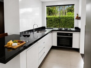 Uma cozinha moderna com bancada preta, armários brancos, forno embutido e janela com vista para o verde.