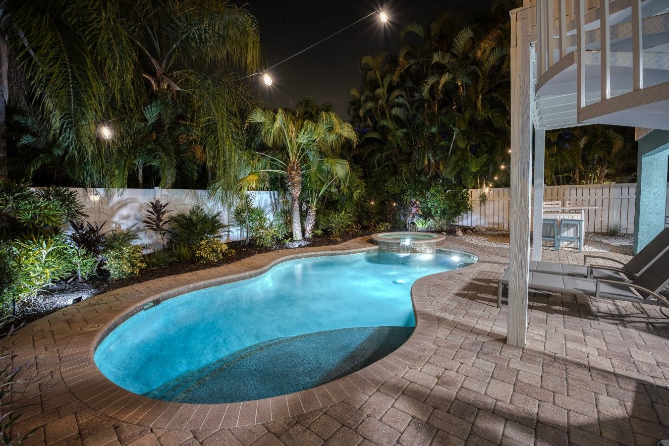Ein Pool mit geschwungener Kante, umgeben von einer Pflasterterrasse und üppiger Bepflanzung.