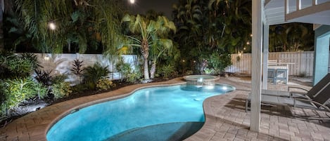 Ein Pool mit geschwungener Kante, umgeben von einer Pflasterterrasse und üppiger Bepflanzung.