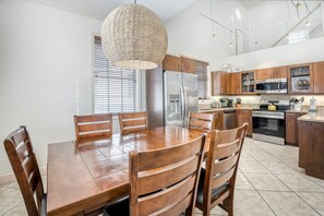 A modern kitchen with wooden cabinets, stainless steel appliances, and a dining area with a wooden table and chairs. - Banana Cabana- Perfect Location (Holmes Beach)