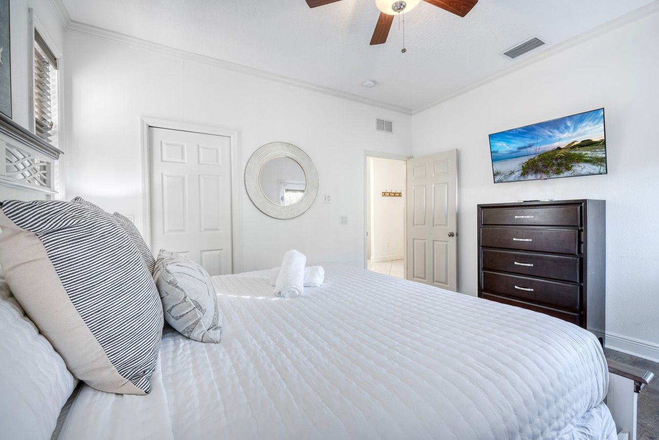 Quarto com cama, penteadeira, ventoinha no teto, espelho e um quadro.