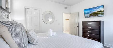 A bedroom with a bed, a dresser, a ceiling fan, a mirror, and a painting.