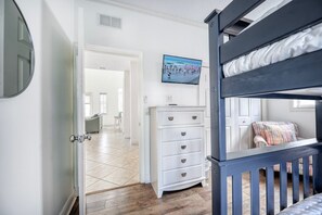 A room with a bunk bed, a white dresser, a television on the wall, and a door leading to another room. - Banana Cabana- Perfect Location (Holmes Beach)