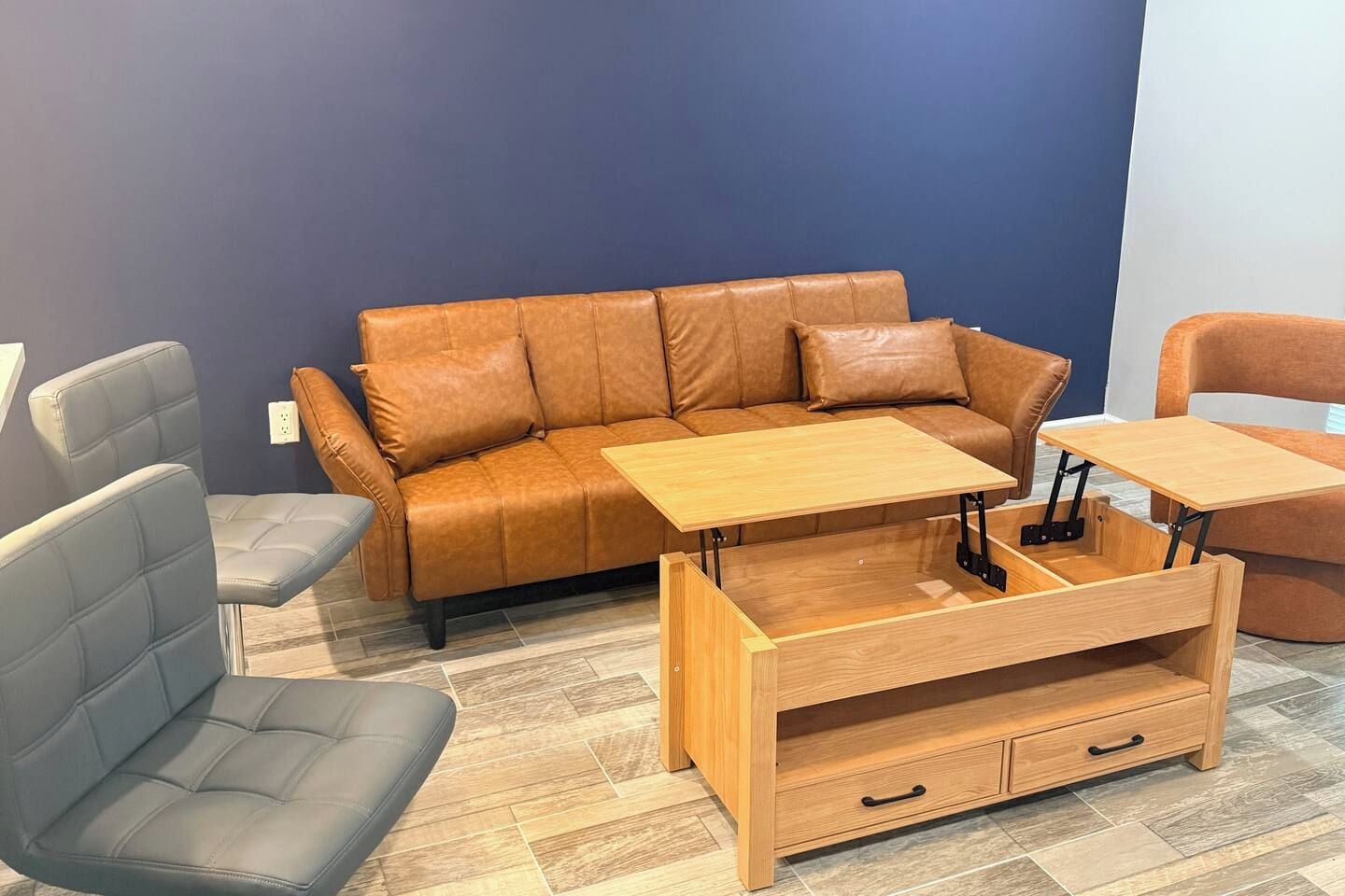A room with a brown leather sofa, a grey armchair, and a wooden coffee table with a drawer.