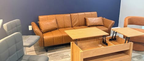A room with a brown leather sofa, a grey armchair, and a wooden coffee table with a drawer.