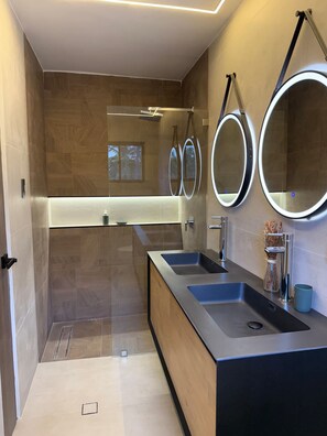 Un baño moderno con dos lavamanos, un espejo y una zona de ducha.