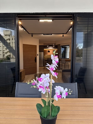 Un interior moderno con una orquídea en maceta sobre una mesa, una zona de comedor y vistas al exterior.
