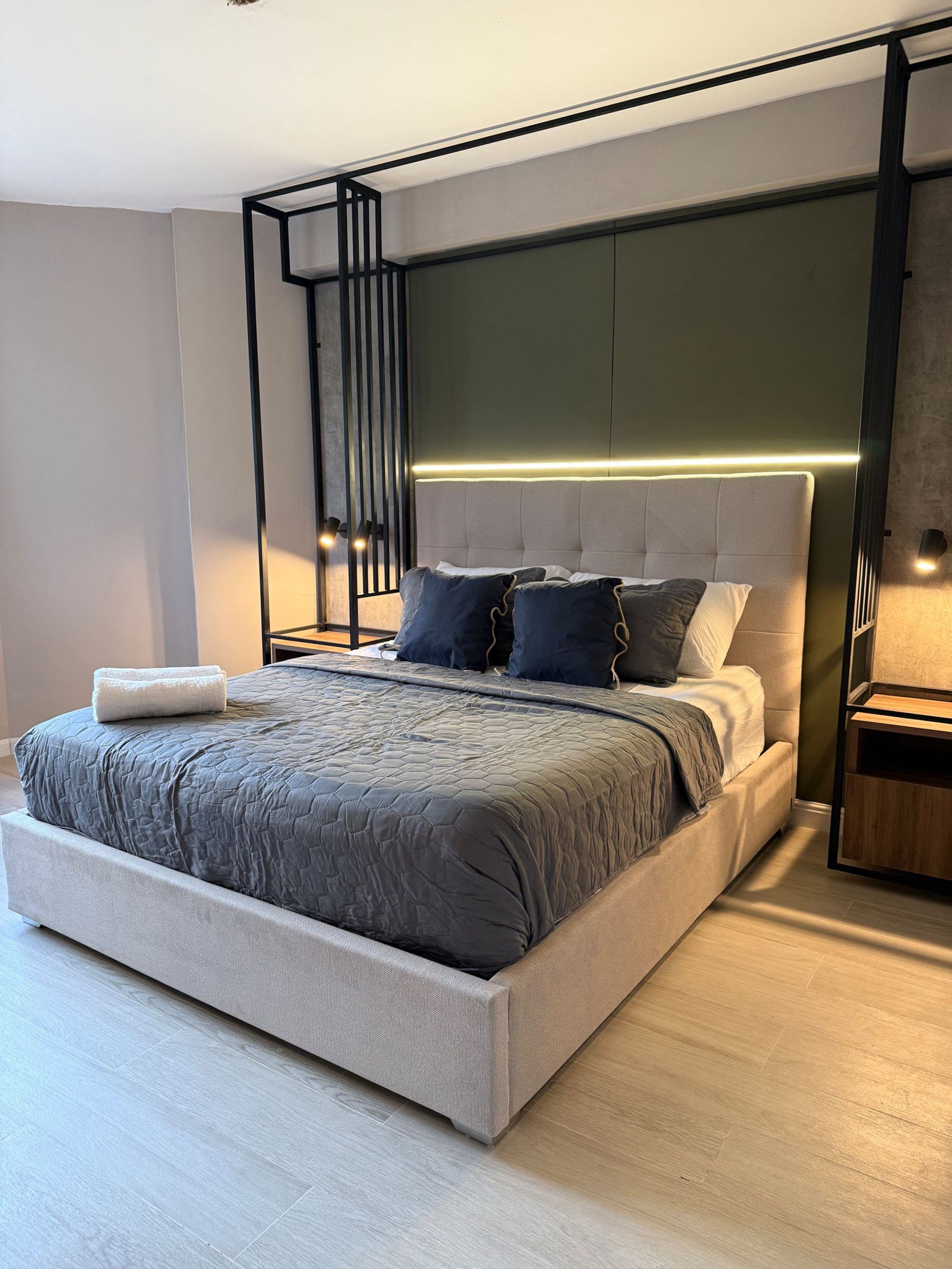 A modern bedroom with a large bed, a headboard with integrated lighting, and a minimalist design.