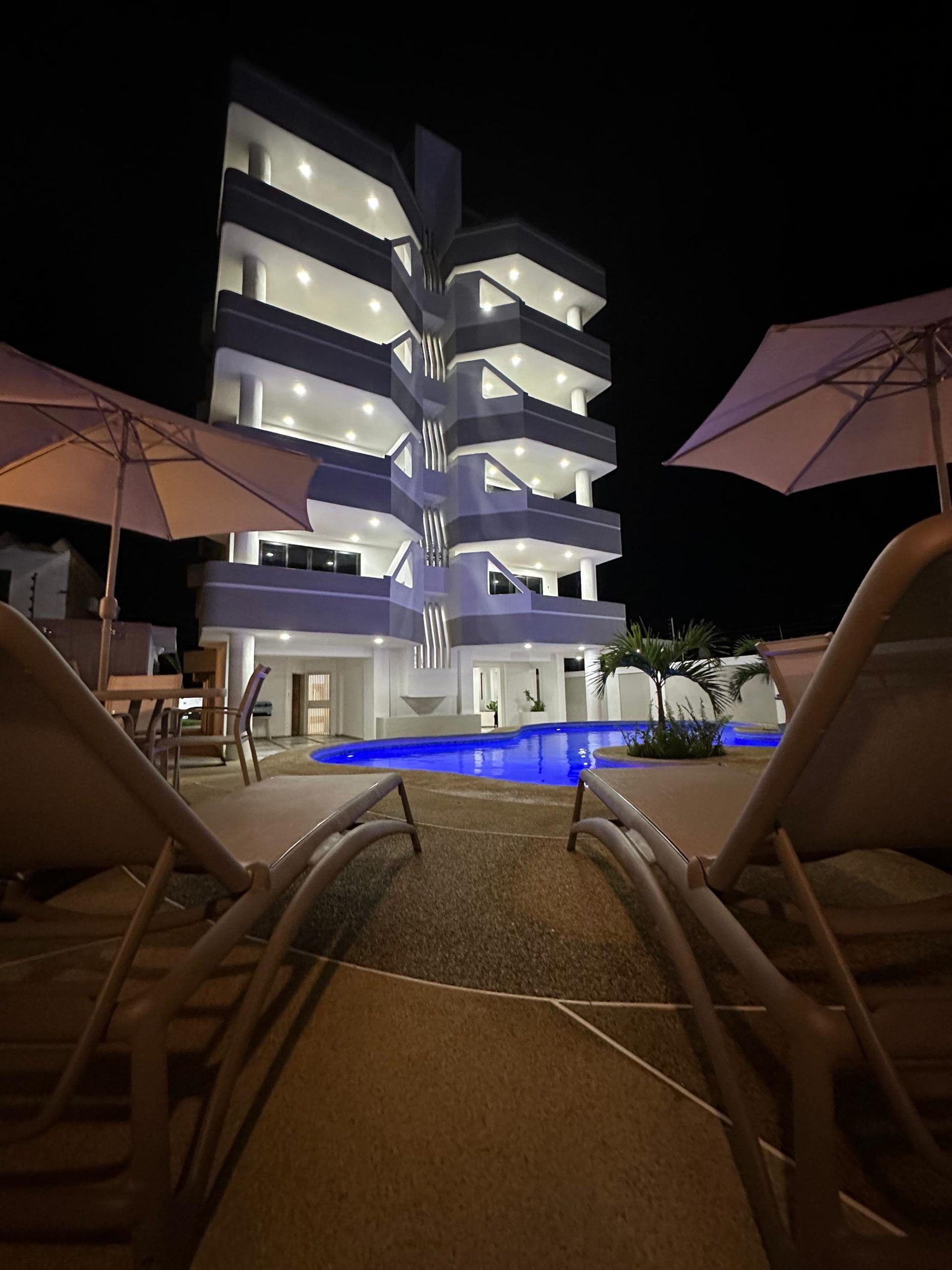 A multi-story hotel with a pool, lounge chairs, and umbrellas.