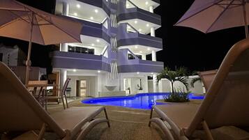 A multi-story hotel with a pool, lounge chairs, and umbrellas.