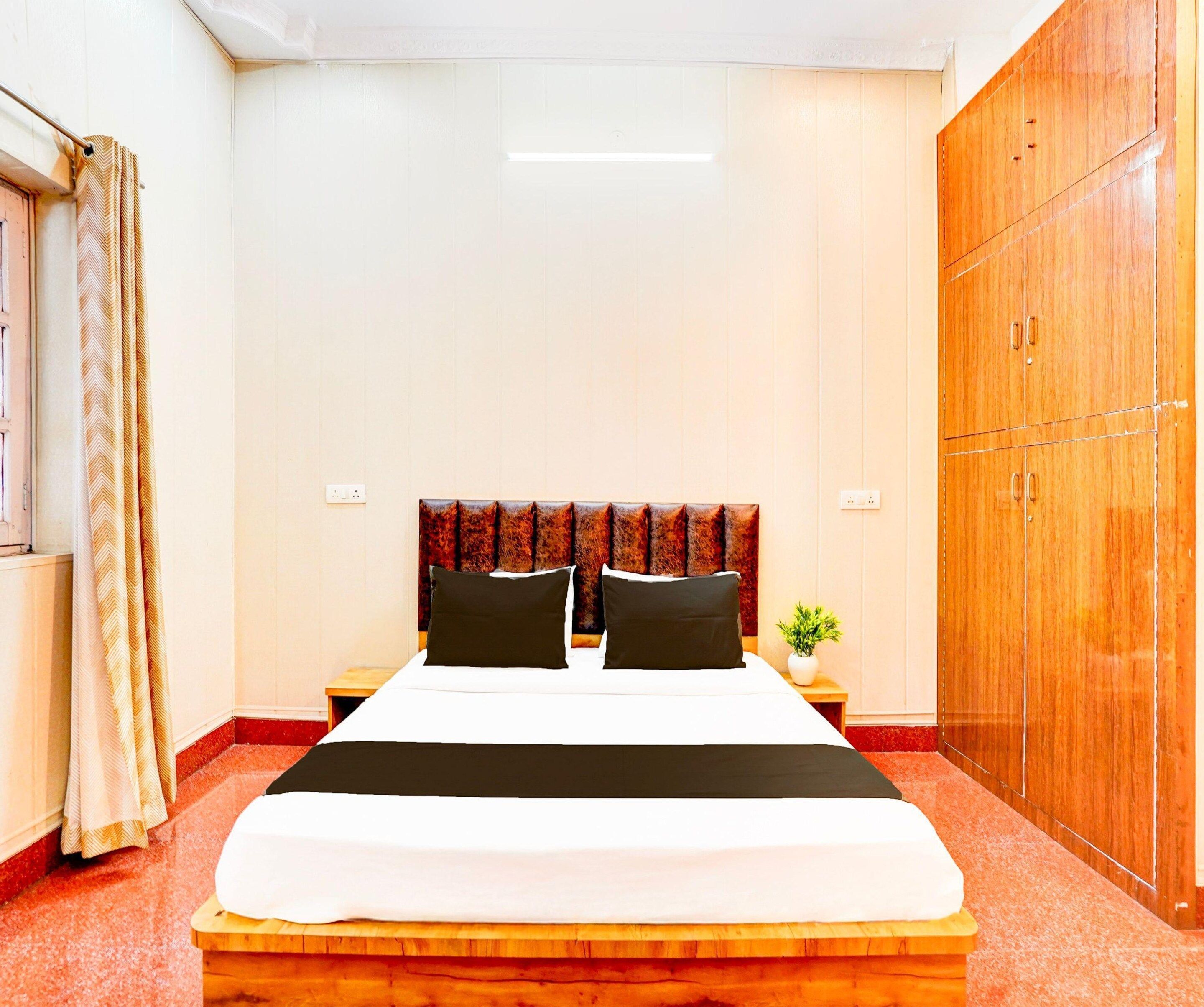Una habitación de hotel con cama, armario, mesita de noche y ventana con cortinas.