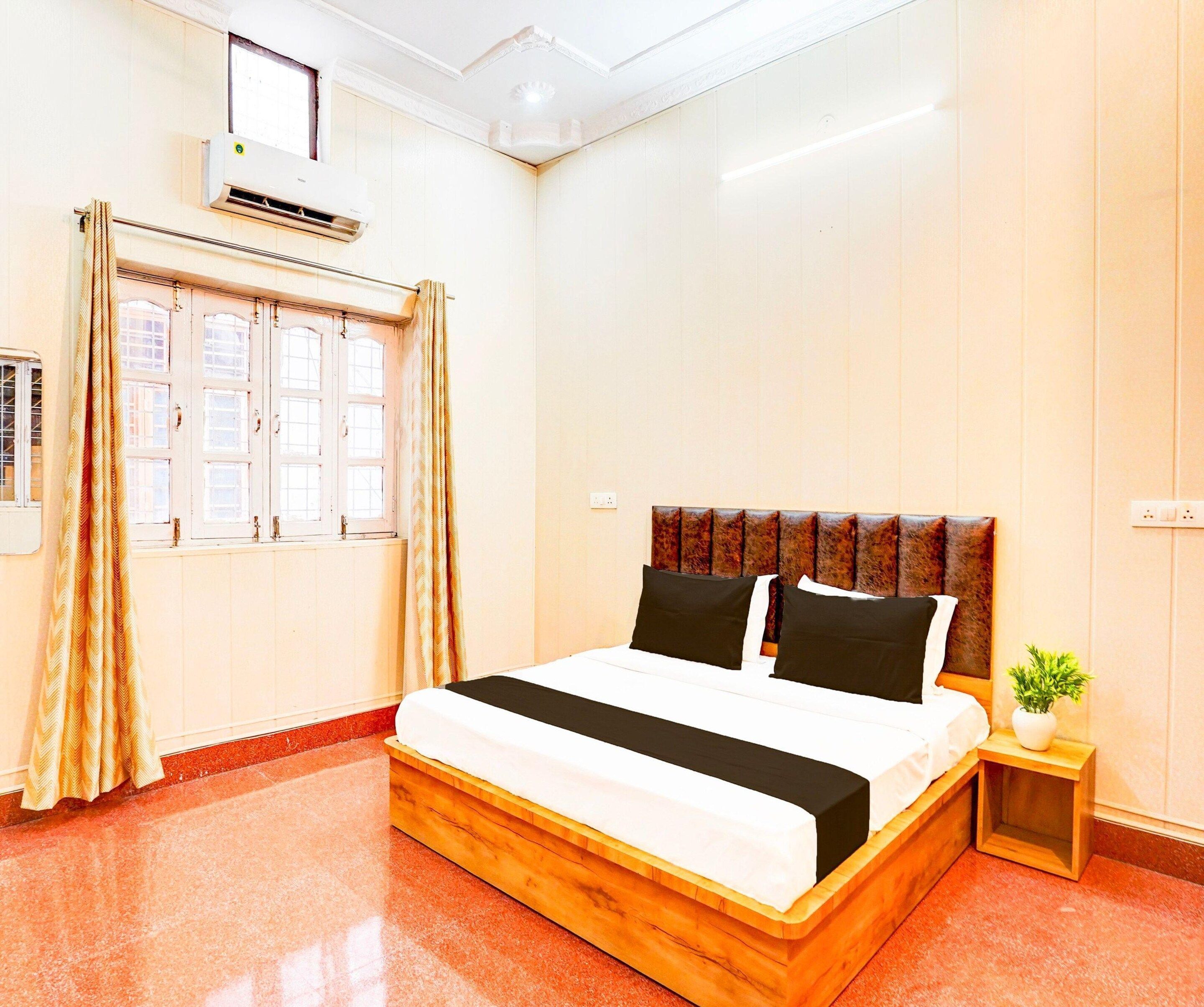 Una habitación de hotel con una cama de madera, una mesita de noche, una planta en maceta y una ventana con cortinas.